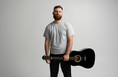 Portrait of handsome young bearded musician, guitar player standing with acoustic guitar in a hand...