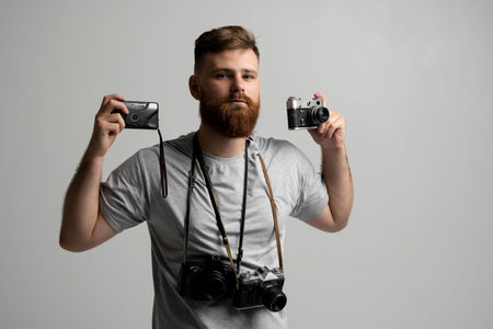 Handsome and confident bearded man photographer with a professional cameras ready in a hand for take...