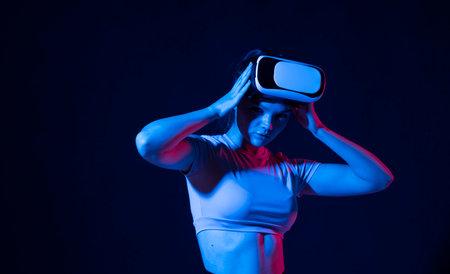Young woman working in VR goggles on a grey background. Modern architect using virtual reality glasses at workplace. Designer working in augmented reality vr studio.の写真素材