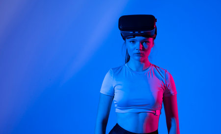 Young brunette woman wearing virtual reality device, vr glasses and playing a game with a friends online in neon light.の写真素材