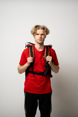 Delivery Service Cocnept. Portrait of male courier wearing red uniform and thermo backpack bag looking at camera isolated on white studio background.の写真素材