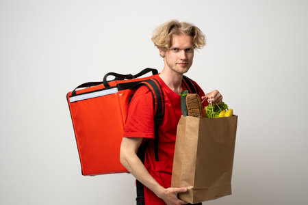 Sive view handsome delivery man, courier carrying package bag of grocery food and drinks from store, supermarket isolated on white studio background.の写真素材