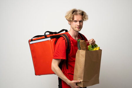 Sive view handsome delivery man, courier carrying package bag of grocery food and drinks from store, supermarket isolated on white studio background.の素材 [FY310205034384]