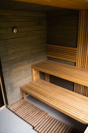 Interior of Finnish sauna, classic wooden sauna with hot steam. Wooden interior baths, wooden benches and loungers, spa complex.の素材 [FY310209036633]