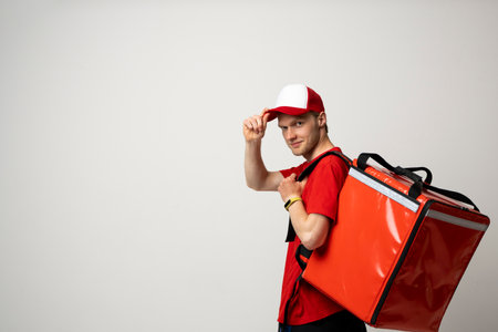 Food Delivery. Side view courier man employee man in red uniform work as courier and hold a red thermal food bag backpack isolated on white background studio.の写真素材