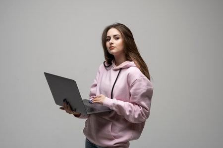 Cheerful young brunette woman standing over grey background using laptop computer.の写真素材
