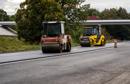 Two heavy asphalt road roller with heavy vibration roller compactor that press new hot asphalt on the roadway on a road construction site.の写真素材