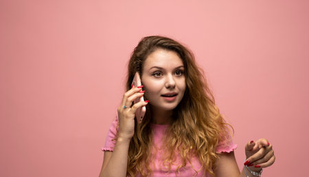 Surprised woman talking on phone with expressive face against pink backgroundの写真素材