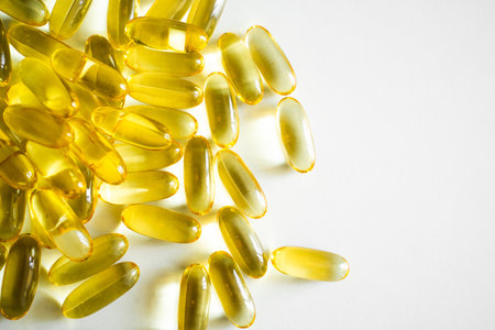 Close-up of scattered yellow fish oil softgel capsules on white backgroundの写真素材