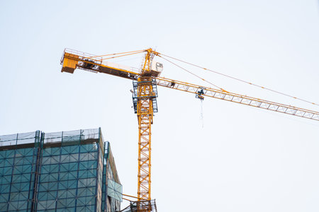 Yellow tower crane rising above skyscraper top under blue skyの写真素材