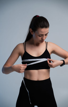 Athletic woman measuring chest with tape in studio, fitness progress, health monitoring and body...