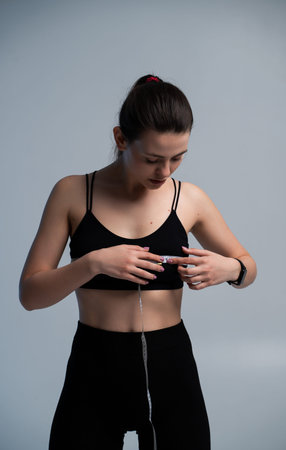 Young adult woman measuring bust size with a measuring tape, practicing self-care for body health, fitness, and weight loss progress, focusing on a healthy lifestyleの写真素材