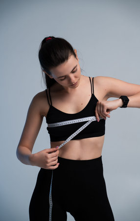 Young woman measuring her body with a tape line, focusing on weight loss progress, healthy lifestyle journey, and fitness goals for a balanced and strong physiqueの写真素材
