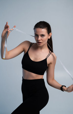 Young woman measuring her body with a tape measure, focusing on fitness, weight loss, healthy lifestyle, and achieving personal body goals with dedicationの写真素材