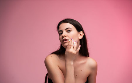 Young woman applying skincare product to her face, using cotton pad for cleansing, focusing on beauty and health with fresh, glowing skin on pink backgroundの写真素材