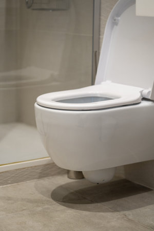 Wall-mounted toilet in a modern bathroom, featuring a white ceramic bowl and lid, emphasizing...
