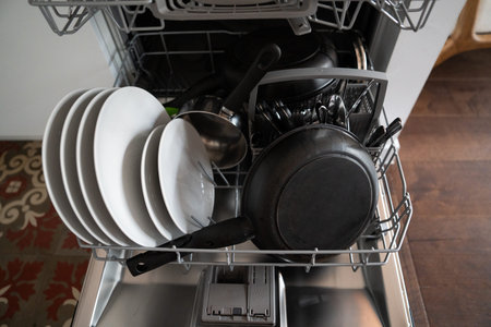 Dishwasher rack filled with clean plates, bowls, frying pan, and cutlery, representing everyday...