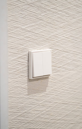 White double light switch on a textured wallpapered wall, representing concepts of electricity, home...