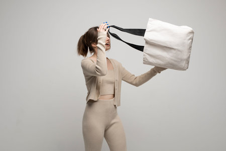 Young woman in beige clothes looking inside large white eco tote bag