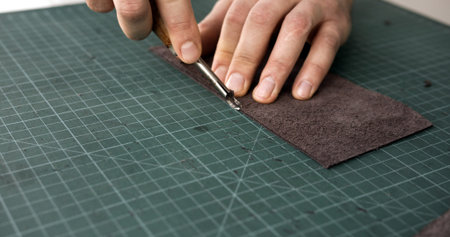 Craftsman using edge tool on leather strip for handmade leather goods production