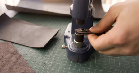 Installing metal snap button on leather piece using press tool in workshop