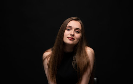 Young woman with long brown hair posing confidently in a studio portrait with a dark background