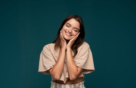 Young woman closing eyes and smiling, hands on face, expressing happiness, joy, and positive emotion...
