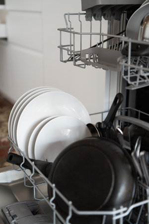 Dishwasher opening with freshly washed plates and pans, showing kitchen organization, hygiene, and...