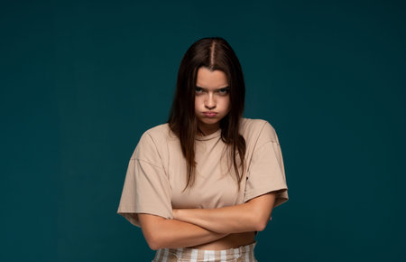 Young angry woman pouting with crossed arms, feeling frustrated and upset on a minimal teal...
