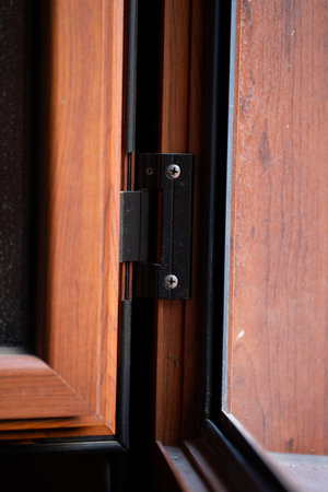 Wooden window frame detail, showing a black metal hinge mechanism and securing screws, contributing...