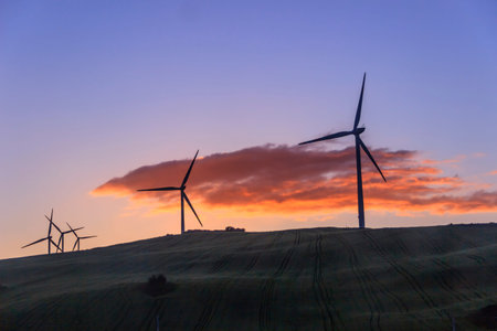 Renewable energy: wind power. Sky at sunset with orange cloud: hilly rural landscape with wind...