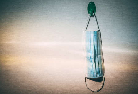 A medical mask hanging on a green hook on the wallの写真素材