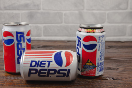 Three old aluminum cans of Pepsi against a white brick wall laying on the wooden table