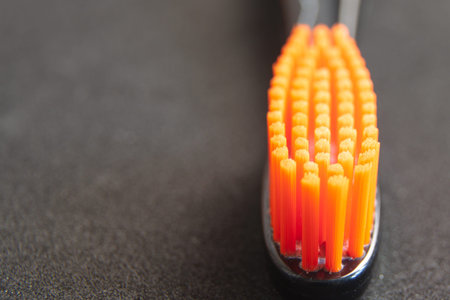 Black head toothbrush with orange bristles close up on black background