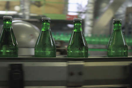 Automatic conveyer belt with green glass bottles for beverages. Concept of producing clean bottled waterの写真素材