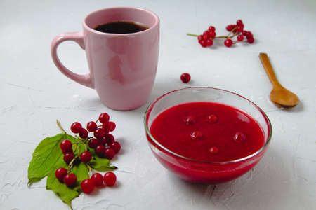An autumn composition with viburnum jam, viburnum branches and leaves, white linen towel, pink cup, and wooden spoonの写真素材