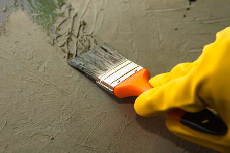 A hand in a yellow glove paints a concrete surface with black oil paint. The concept of DIYの写真素材