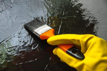 Hand with a brush in a yellow rubber glove, paints with black paint. The concept of creative designの写真素材