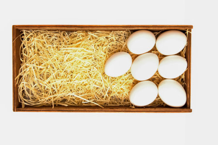 White chicken eggs lie on straw in a wooden box, isolated on a white background. The view from the topの写真素材