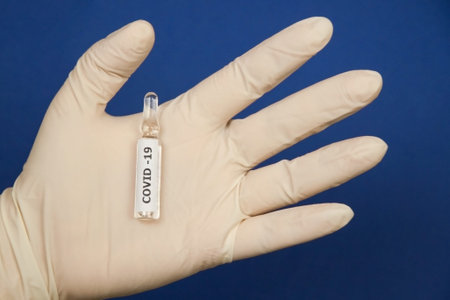 In the hand in a medical glove is an ampoule with a vaccine. Close-up