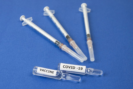 Syringes and ampoules with the Covid-19 vaccine lie on a blue background. Close-upの写真素材