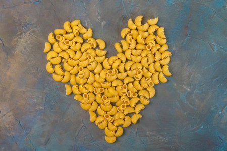 Raw elbows pasta in a shape of heart laying on a moody dark background. The concept of Valentine's Dayの写真素材