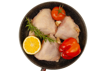Raw chicken thighs laying in grill pan with lemon, bell pepper, greens and garlic isolated on white background. Top viewの写真素材