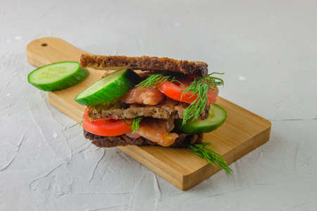 Redfish bread sandwich with cucumber and tomatoes for breakfast laying on a wooden board. Concept of a healthy foodの写真素材