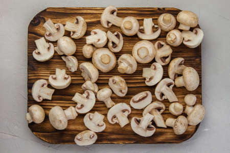 Whole and sliced champignons lie on a burnt wooden board. Top viewの写真素材