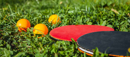 Two table tennis rackets and three orange balls lie in the grass. The concept of outdoor sports gamesの写真素材
