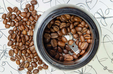Electric coffee grinder with freshly roasted coffee beans on the background of a handful of coffee beans on the table. Top viewの写真素材