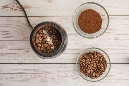 Coffee beans in the mill and grounded coffe in the bowl on the wooden background top viewの写真素材