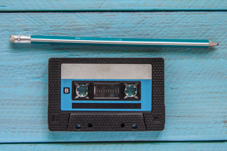 A black audiotape and a simple green pencil lie on a blue wooden background. Top view