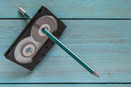 On a blue wooden background is an audio tape with a pencil threaded through it. Space for the text. Close-upの写真素材